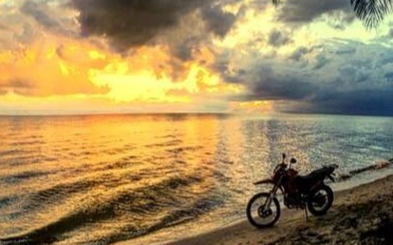 A motorbike in front of the ocean at sunset