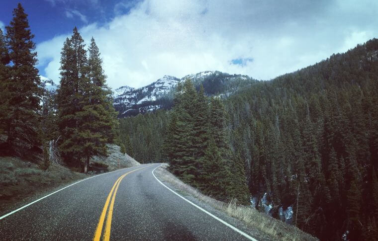 A clear mountain highway, surrounded by snowcapped mountains and pine trees.