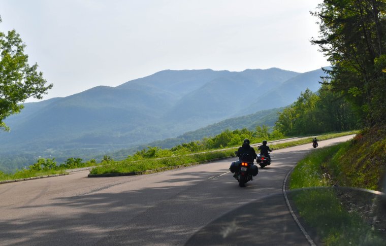 Two motorcyclists turning on a bend with a backdrop of the green Smoky Mountains.
