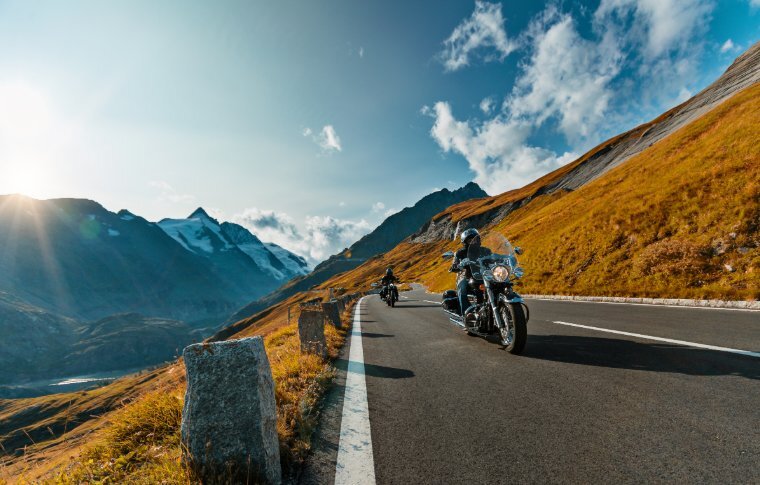 Two motorcyclists riding through the mountains, snowcapped mountains in the background.